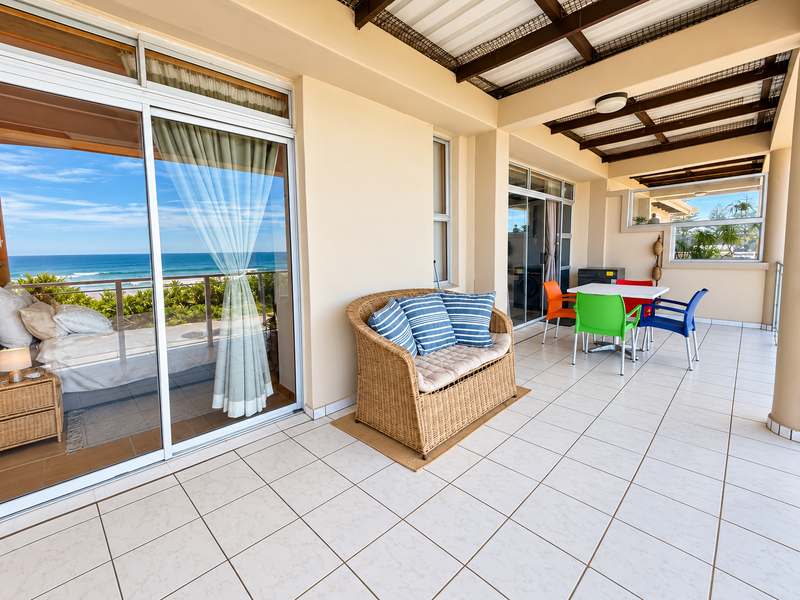 Spacious covered balcony featuring tiled flooring, exposed beam ceiling, and large sliding glass doors with direct ocean views.
