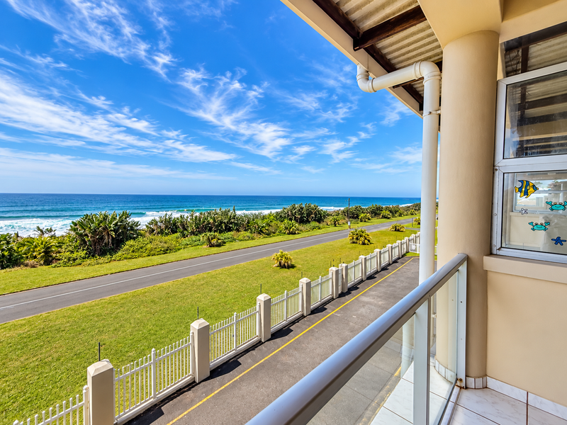 A spacious balcony featuring a glass balustrade and tiled flooring, offering expansive views of the coastal road and ocean.