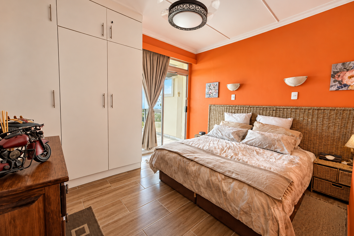 A bright bedroom featuring built-in cupboards, tiled flooring, and a sliding glass door providing access to an outdoor balcony area.