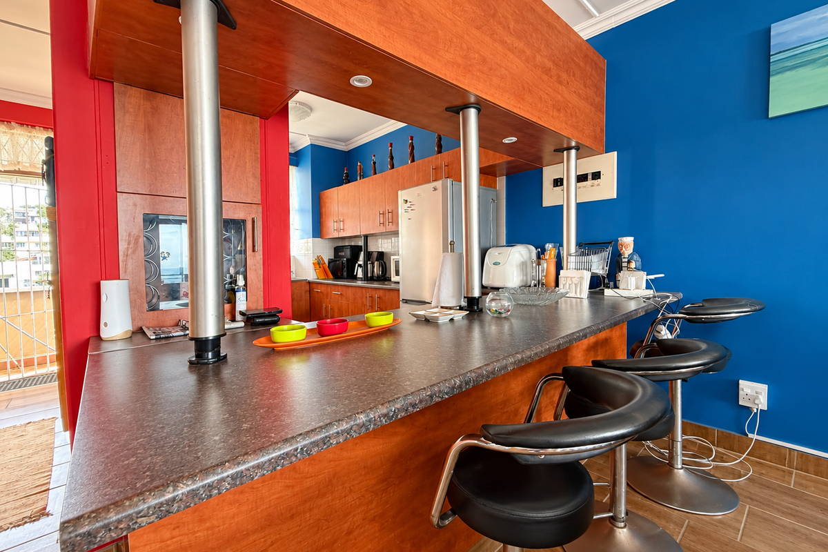 A kitchen featuring a wooden breakfast bar with metal supports, ample cabinetry, and tiled flooring, set against vibrant blue and red accent walls.