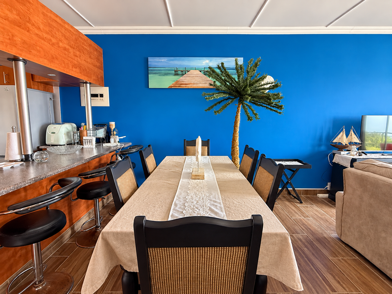 Open plan living and dining area featuring a breakfast bar, wood-look laminate flooring, and a distinctive blue accent wall.