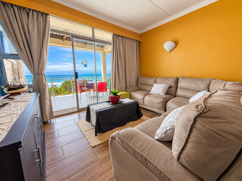 A bright living room featuring tiled floors, crown molding, and large sliding glass doors that open onto a balcony with ocean views.