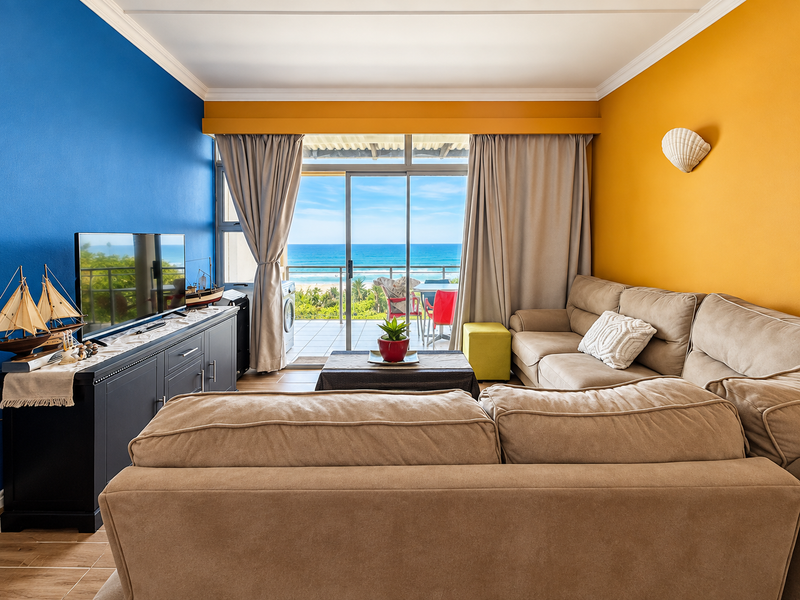 A bright living room featuring vibrant accent walls, tiled flooring, and large sliding glass doors that open to a balcony with ocean views.