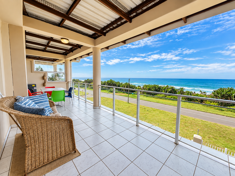 Spacious covered balcony featuring tiled flooring and a glass balustrade, offering expansive ocean and coastal views.