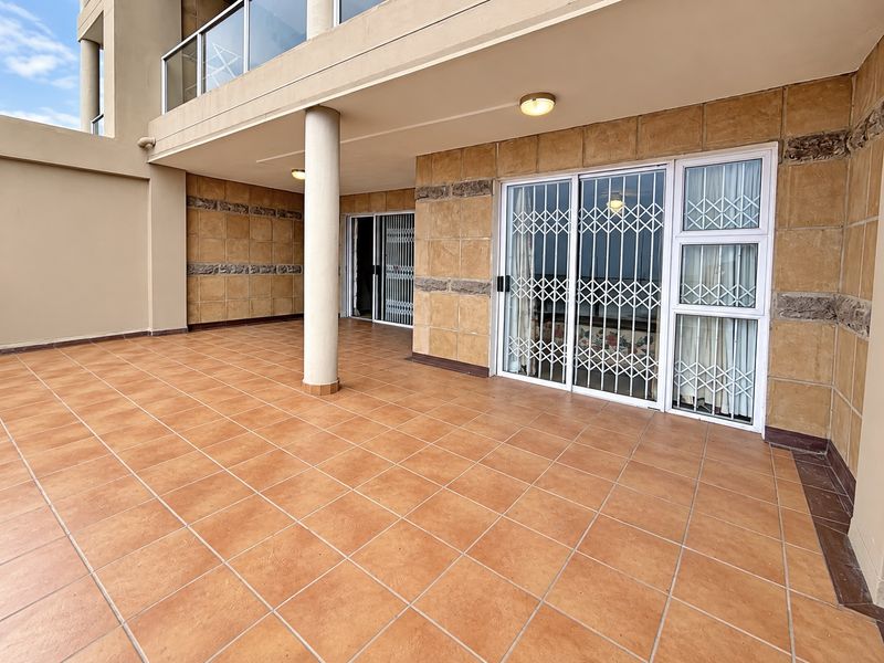 Spacious covered balcony featuring tiled flooring, stone-look wall cladding, and secure sliding glass door access to the apartment interior.