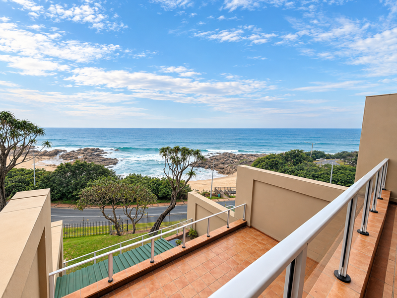 A spacious balcony offering panoramic ocean and coastal views, featuring tiled flooring and a modern safety railing.