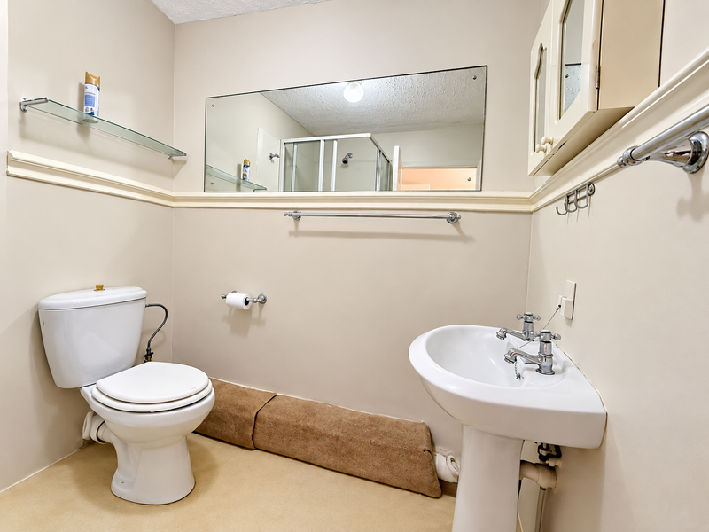 A functional bathroom featuring a pedestal sink, toilet, wall-mounted mirror, and built-in medicine cabinet with neutral wall finishes.