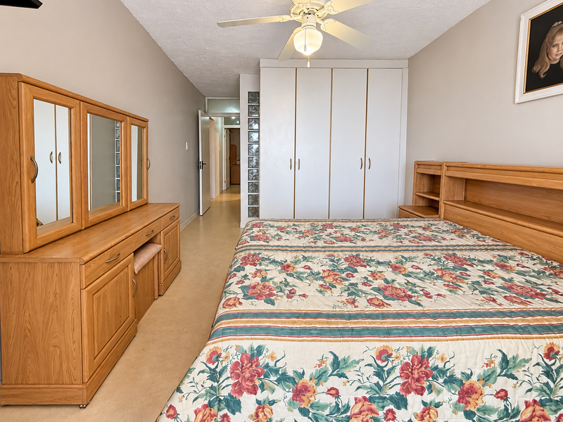 A spacious bedroom featuring built-in cupboards, a ceiling fan, and a unique glass block feature wall, offering a functional layout.