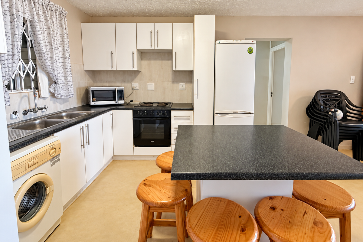 Functional kitchen featuring white cabinetry, dark laminate countertops, a central island, and integrated cooking appliances with a tiled backsplash.