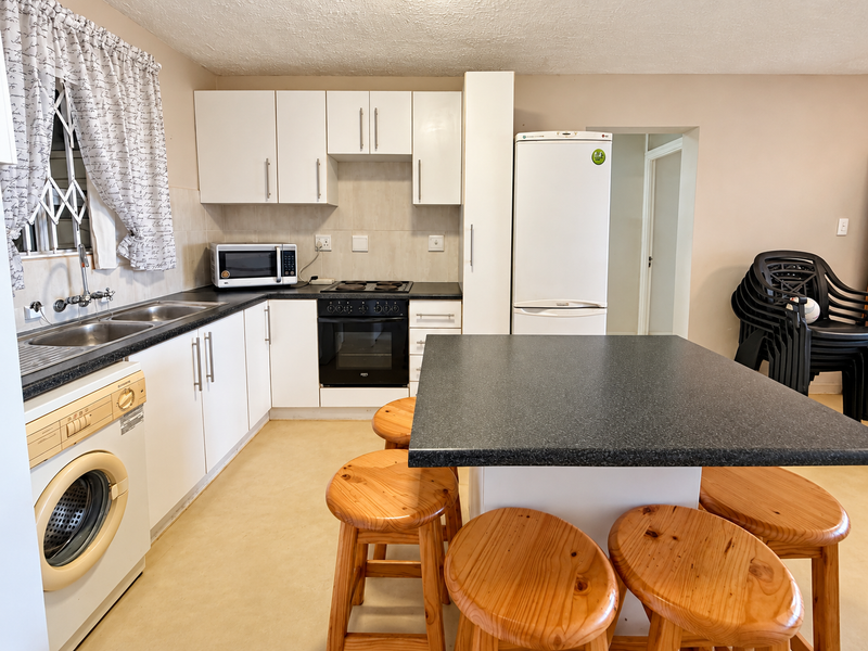 Functional kitchen featuring white cabinetry, dark laminate countertops, a central island, and integrated cooking appliances with a tiled backsplash.