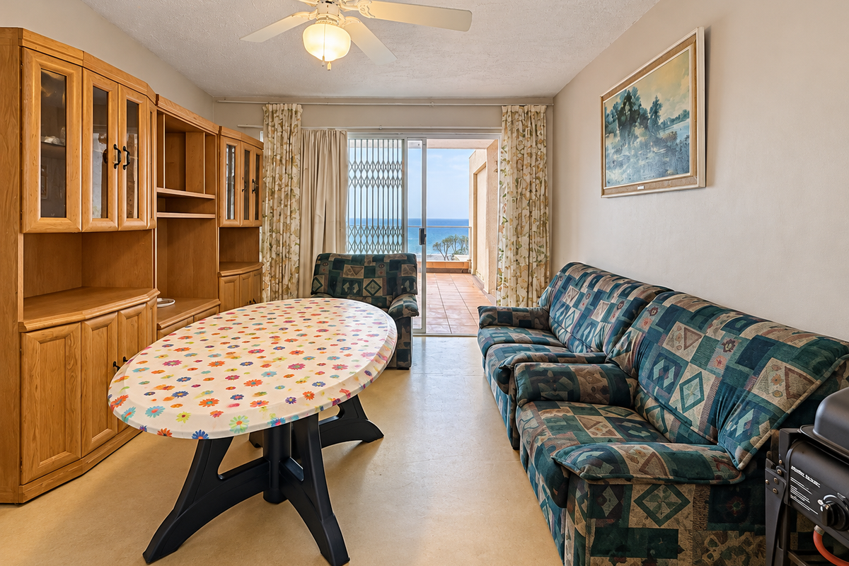 Living room featuring a ceiling fan, tiled flooring, and a sliding glass door leading to a balcony with ocean views.