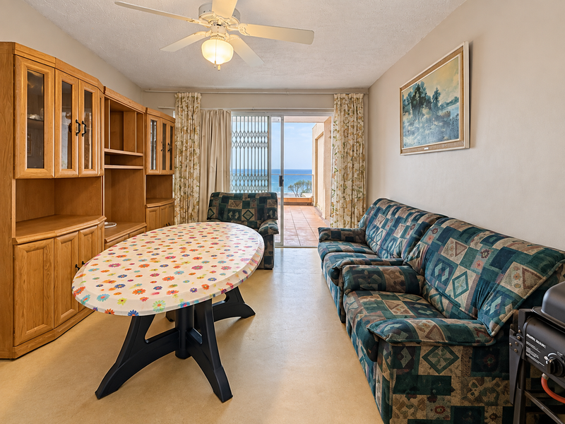 Living room featuring a ceiling fan, tiled flooring, and a sliding glass door leading to a balcony with ocean views.
