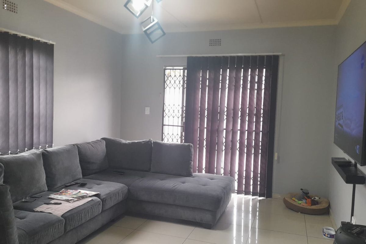 A living room featuring tiled flooring, vertical blinds, and a security gate leading to an outdoor area.