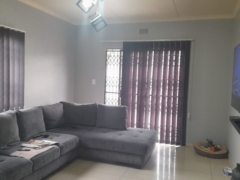 A living room featuring tiled flooring, vertical blinds, and a security gate leading to an outdoor area.