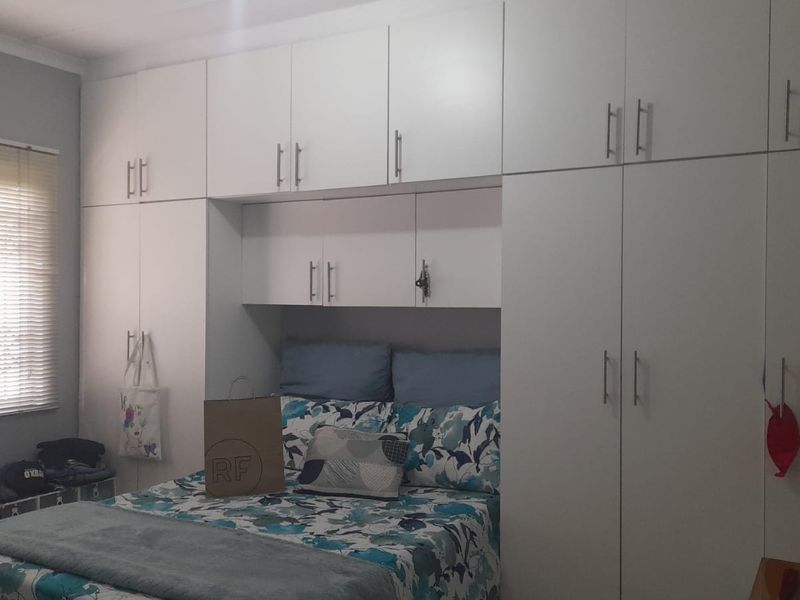 A bedroom featuring extensive white built-in cupboards providing ample storage space and venetian blinds on the window.