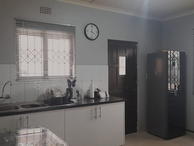 A functional kitchen featuring white cabinetry, a double sink with tiled backsplash, and security bars on the windows.