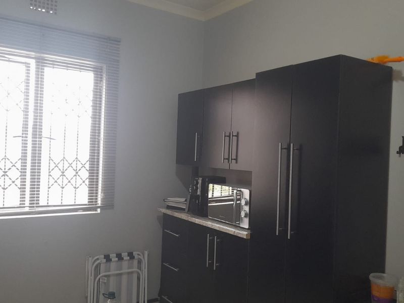 A functional kitchen area featuring dark built-in cabinetry, stone countertops, and a window fitted with security bars and blinds.