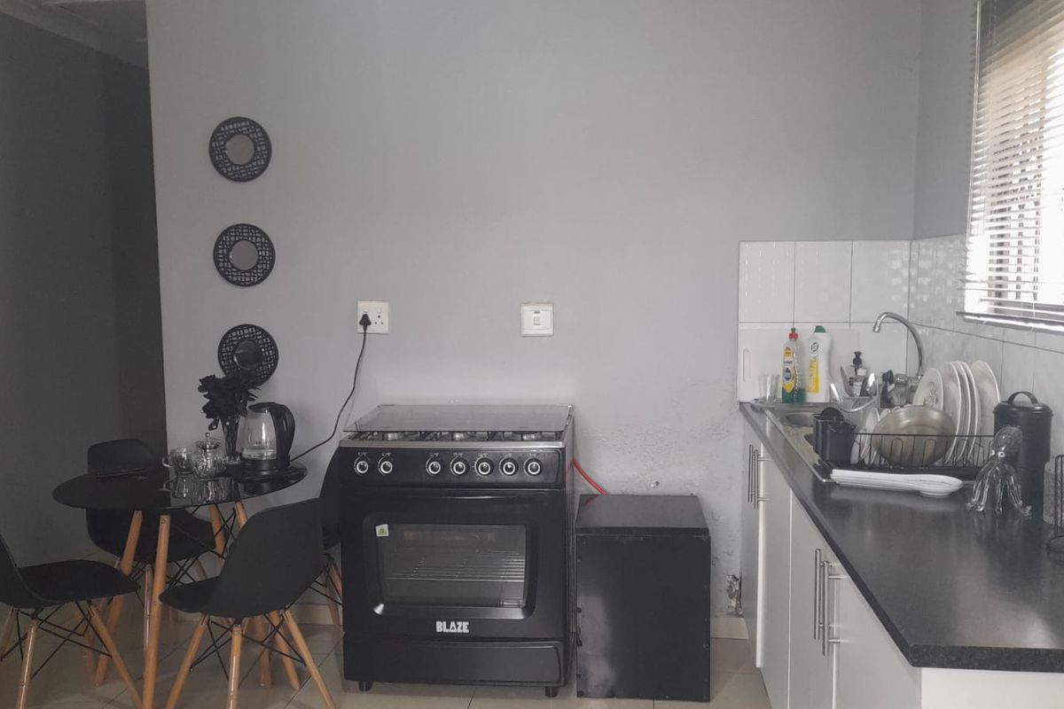 Compact kitchen featuring white cabinetry, dark countertops, tiled splashback, and a freestanding stove, providing a functional cooking and preparation space.
