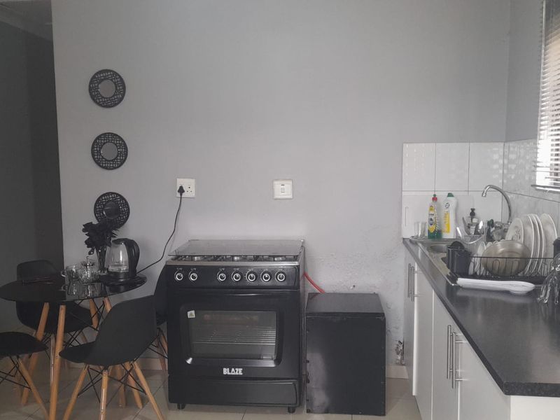 Compact kitchen featuring white cabinetry, dark countertops, tiled splashback, and a freestanding stove, providing a functional cooking and preparation space.