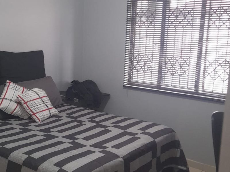 A functional bedroom featuring tiled flooring, security burglar bars on the window, and neutral wall finishes.