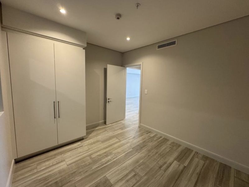 A clean, modern bedroom featuring wood-look tile flooring, built-in wardrobe storage, and recessed lighting, presenting a neutral and well-maintained space.