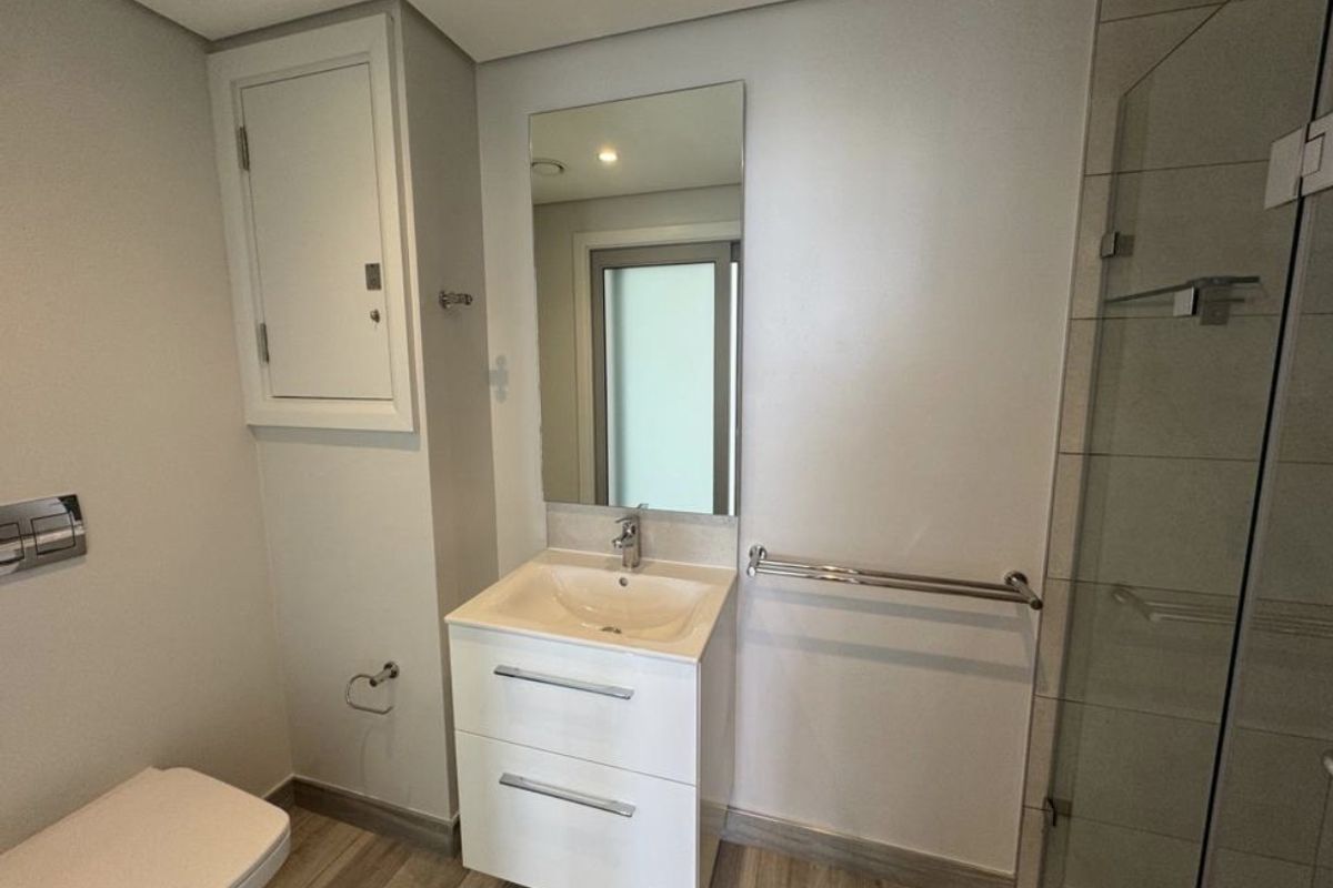Modern bathroom featuring a wall-mounted toilet, vanity cabinet with integrated sink, and a glass-enclosed shower with neutral tile finishes.