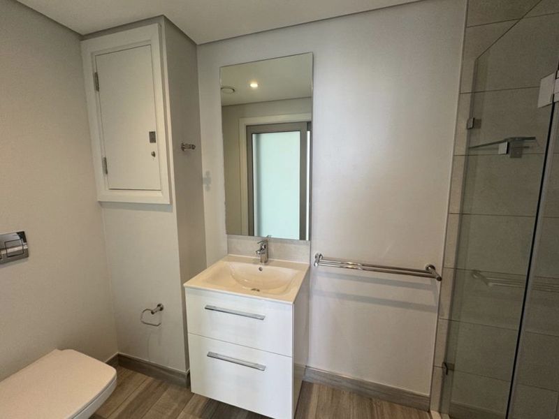 Modern bathroom featuring a wall-mounted toilet, vanity cabinet with integrated sink, and a glass-enclosed shower with neutral tile finishes.