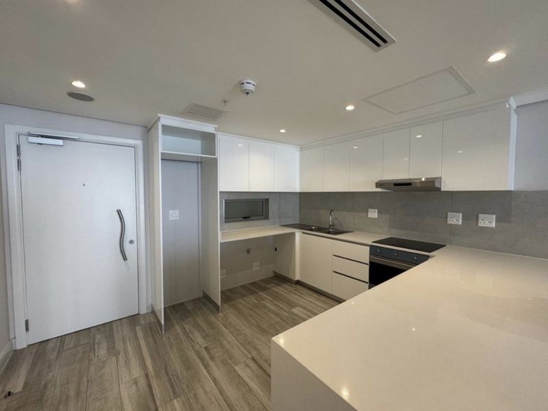 Modern kitchen featuring sleek white cabinetry, stone countertops, integrated appliances, and wood-look flooring in a clean, contemporary apartment setting.
