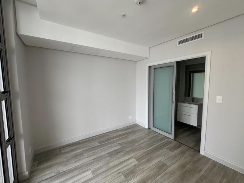 A modern, empty bedroom featuring wood-look tile flooring, recessed lighting, and a sliding frosted glass door leading to an en-suite bathroom.