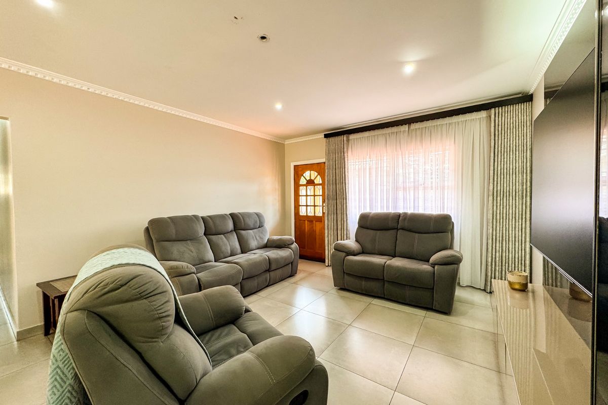 A bright living room featuring tiled flooring, recessed downlighting, decorative crown molding, and a wooden front door with glass paneling.