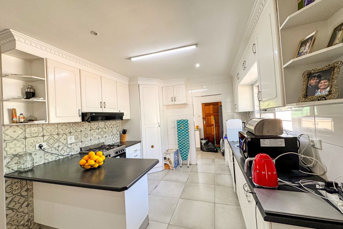 A functional kitchen featuring white cabinetry, patterned tile backsplash, dark countertops, and a gas hob with an integrated extractor fan.