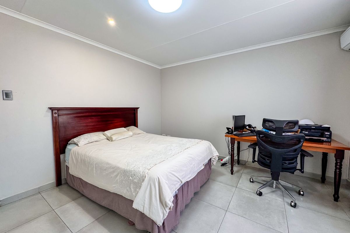A functional bedroom featuring neutral tiled flooring, a wall-mounted air conditioning unit, and recessed ceiling lighting.