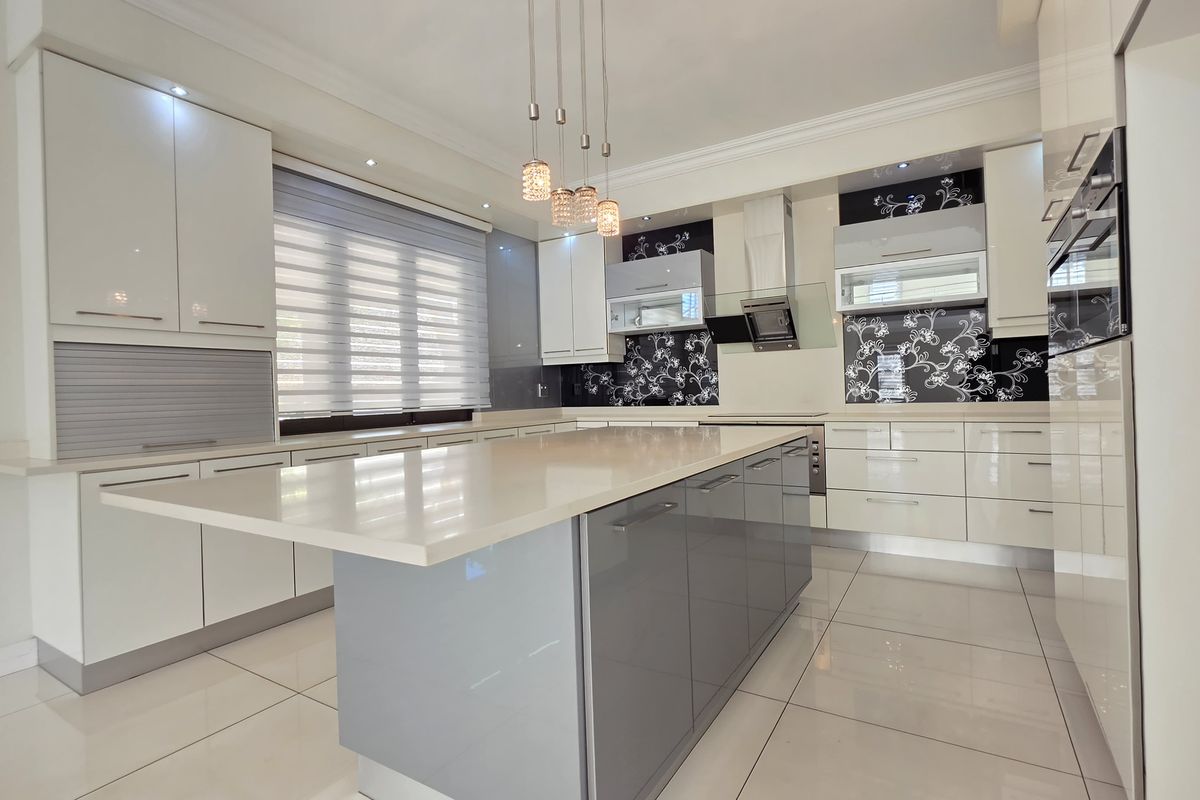 Modern kitchen featuring a large central island, high-gloss cabinetry, stone countertops, integrated appliances, and decorative patterned splashbacks.