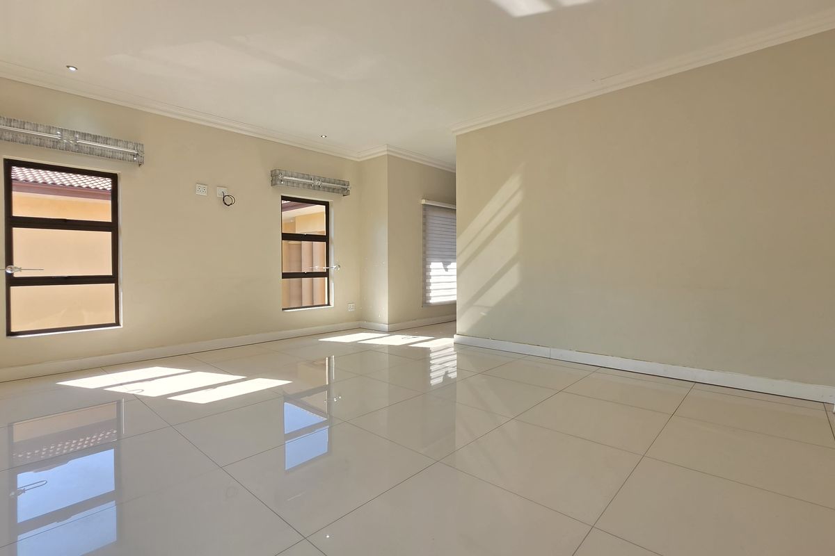 A bright and spacious living area featuring large porcelain floor tiles, neutral wall finishes, and modern aluminium-framed windows.