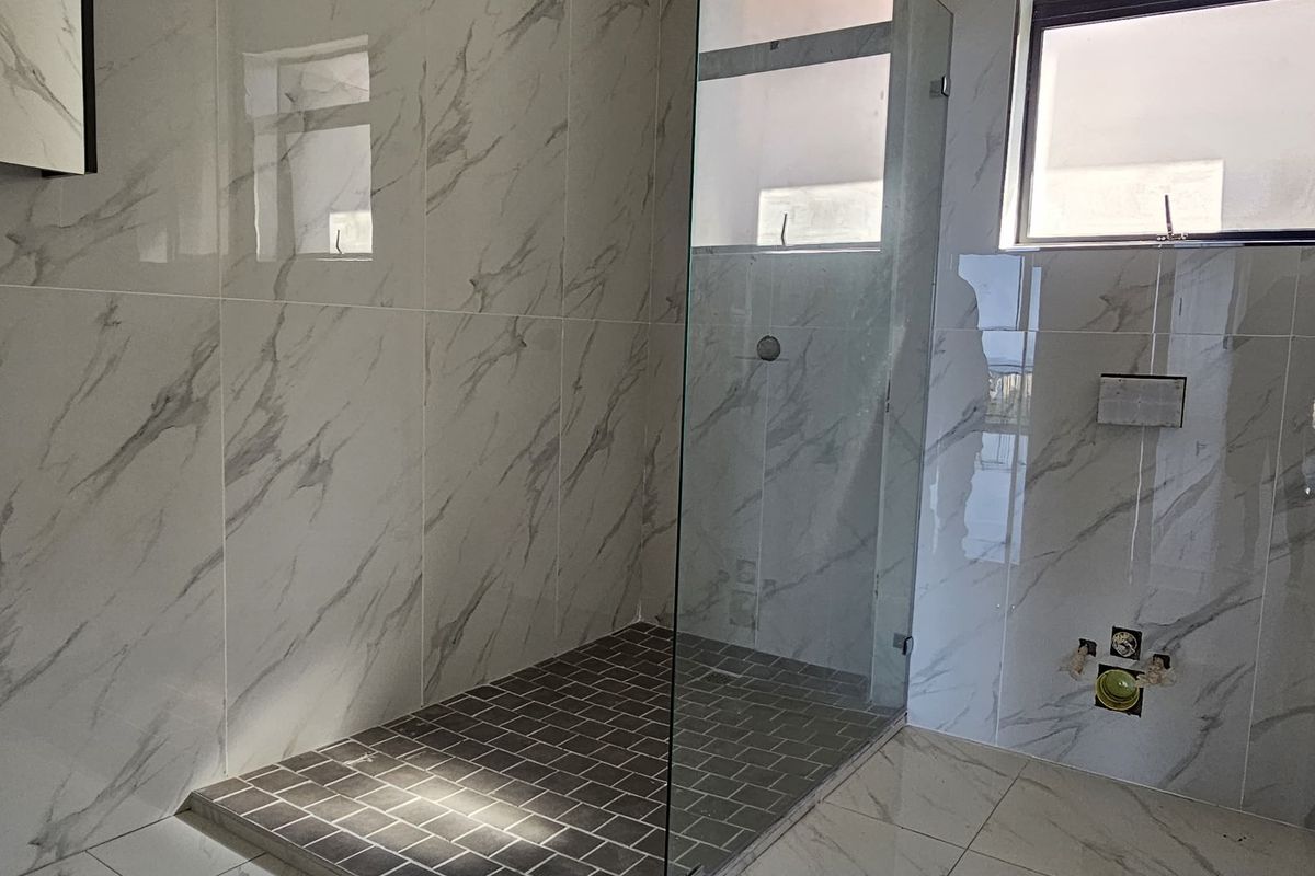 Modern bathroom featuring large format marble-look wall and floor tiles, a walk-in glass shower enclosure with dark mosaic floor tiling, and window ventilation.