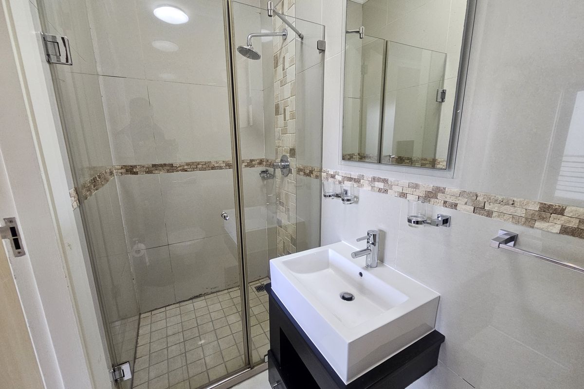 Modern bathroom featuring a glass-enclosed shower, contemporary vanity with a basin, and neutral wall tiling with decorative mosaic accents.