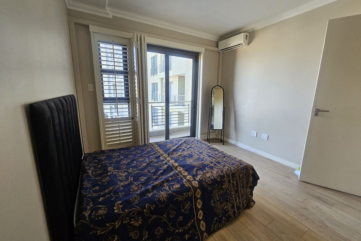 A well-maintained bedroom featuring light wood-look flooring, a wall-mounted air conditioning unit, and sliding glass doors leading to a private balcony.