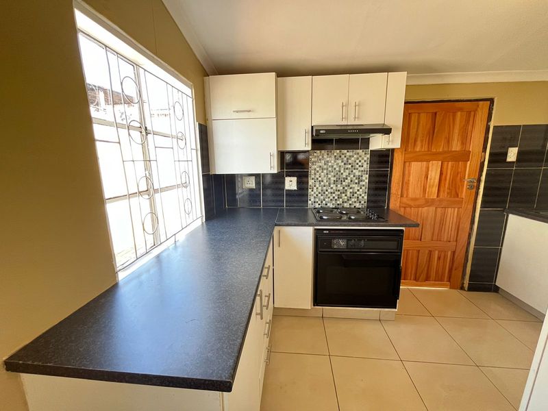 A functional kitchen featuring white cabinetry, dark laminate countertops, a built-in oven with hob, and tiled splashbacks.