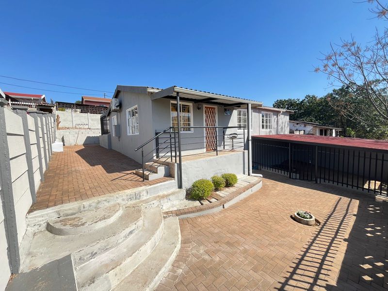 Rear exterior view of the house featuring a paved courtyard, covered patio area, concrete steps, and secure perimeter fencing.