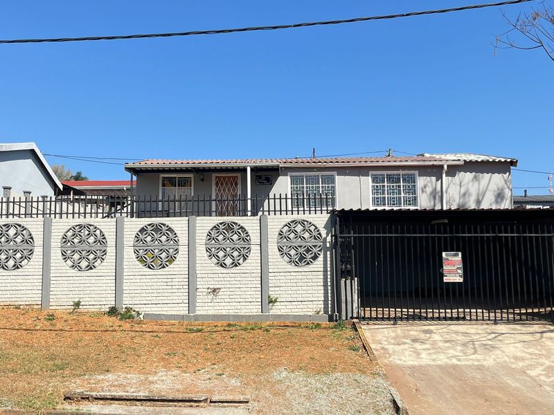 Front elevation of a single-story house featuring a brick boundary wall with decorative screen blocks, a metal driveway gate, and security fixtures.