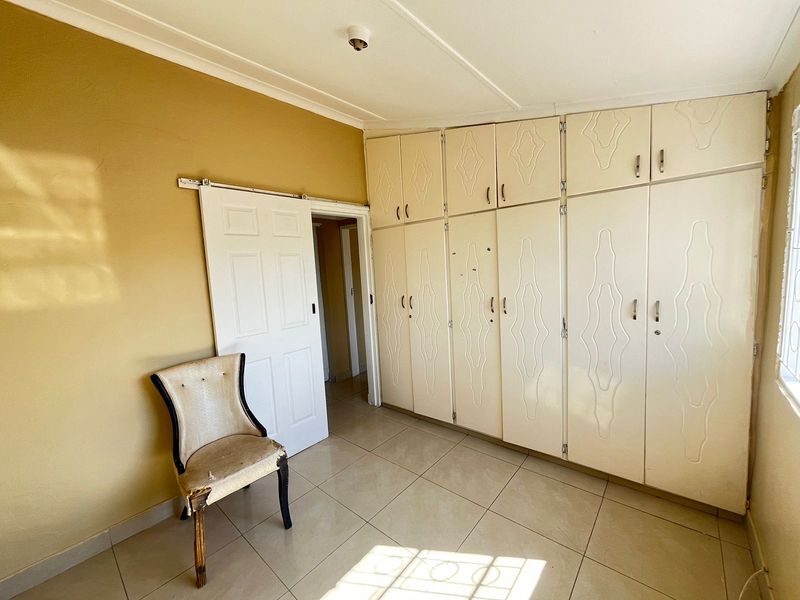 A bedroom featuring extensive built-in cupboards, tiled flooring, and a sliding door, offering a functional space ready for cosmetic updates.
