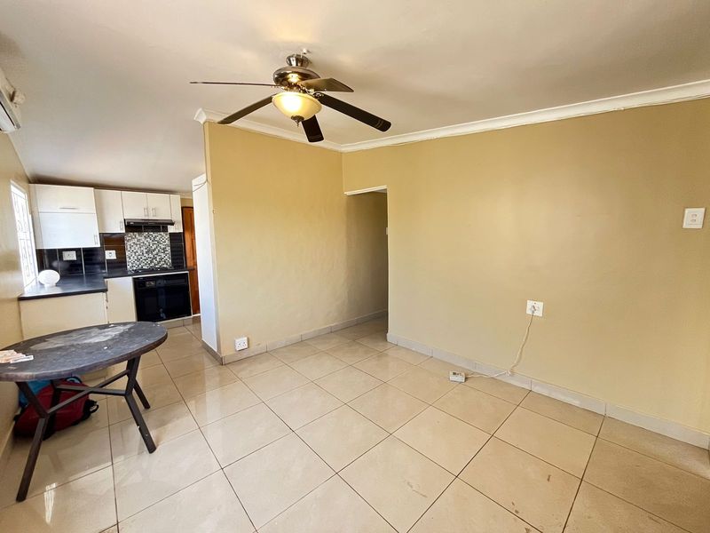 Open plan living area featuring tiled flooring, a ceiling fan, and an adjoining kitchen with built-in cabinetry, oven, and extractor fan.