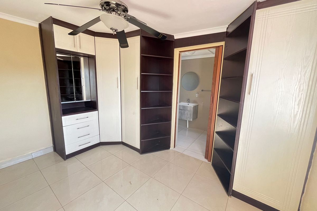 A spacious bedroom featuring extensive built-in cabinetry, a ceiling fan, and tiled flooring, with direct access to an en-suite bathroom.