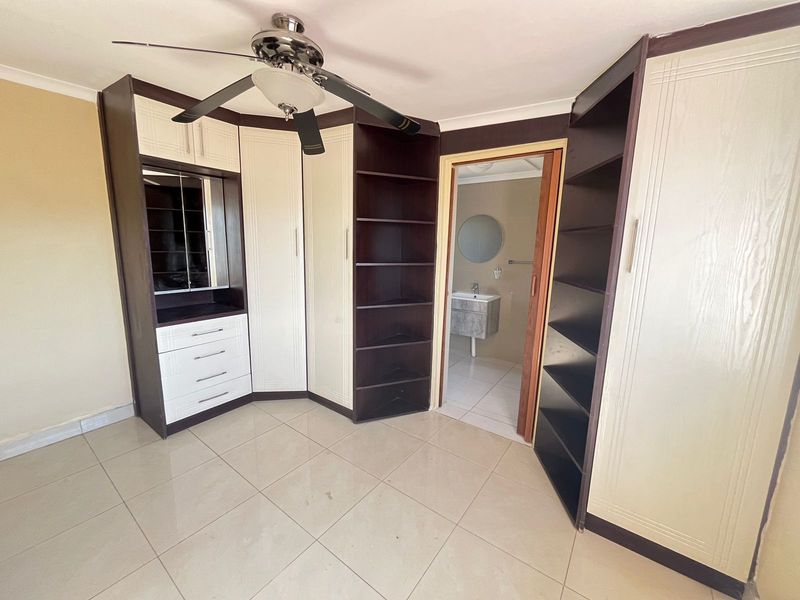 A spacious bedroom featuring extensive built-in cabinetry, a ceiling fan, and tiled flooring, with direct access to an en-suite bathroom.