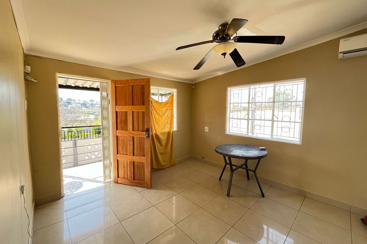 A bright, tiled living area featuring a ceiling fan, air conditioning unit, and direct access to an outdoor balcony through a wooden door.