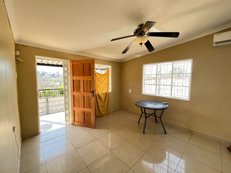 A bright, tiled living area featuring a ceiling fan, air conditioning unit, and direct access to an outdoor balcony through a wooden door.