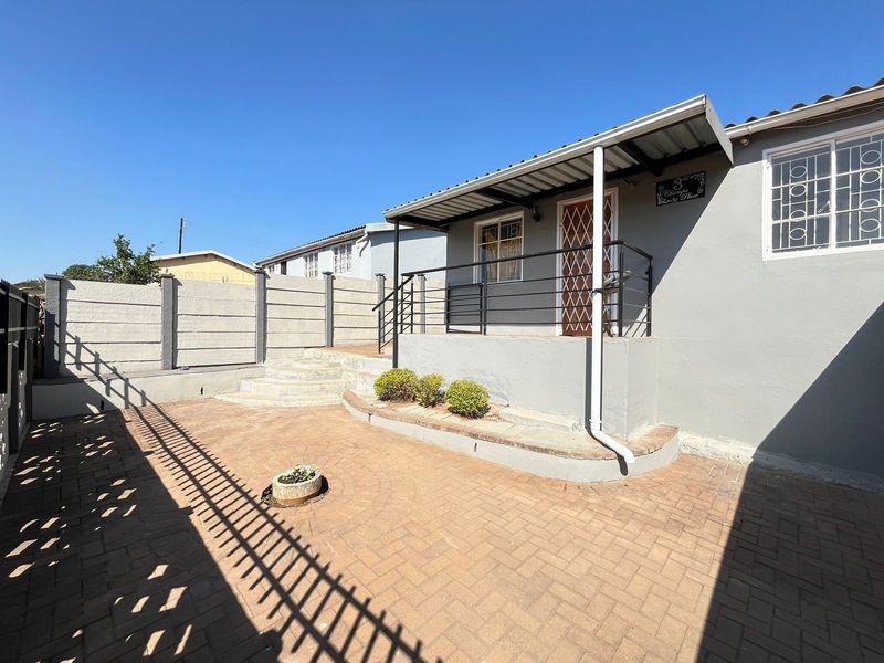 A well-maintained rear exterior area featuring a paved patio, a covered entrance porch, and secure boundary walling.