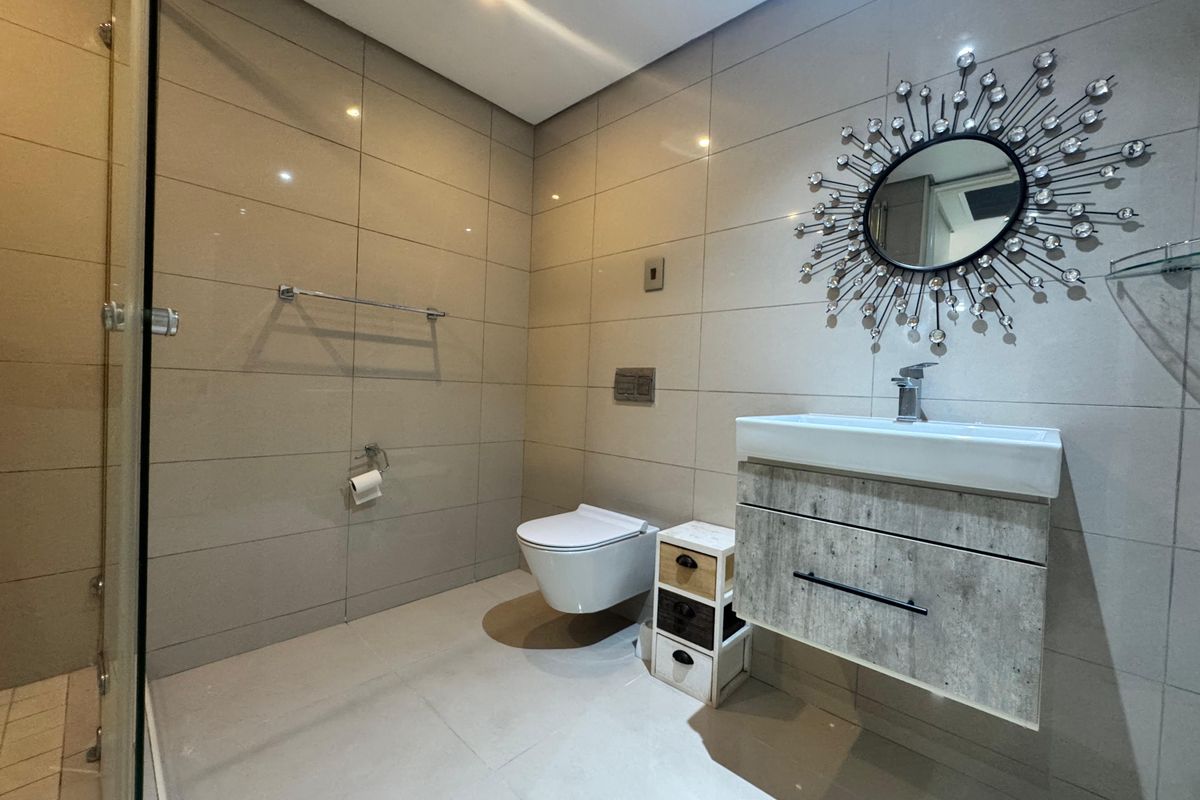 Modern bathroom featuring a wall-mounted vanity, floating toilet, and large format wall tiles with a glass-enclosed shower area.