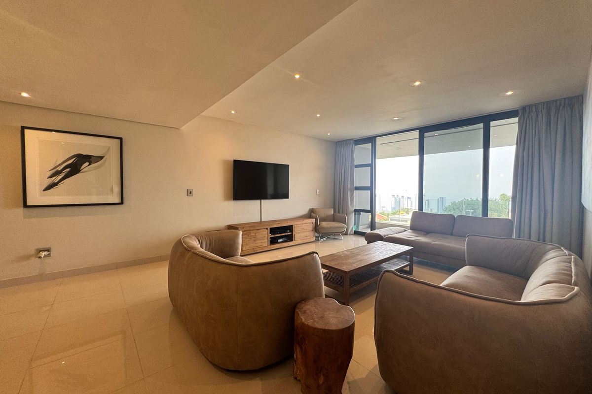 Spacious living room featuring large floor-to-ceiling windows, recessed ceiling lighting, and neutral tiled flooring, offering a bright and comfortable atmosphere.
