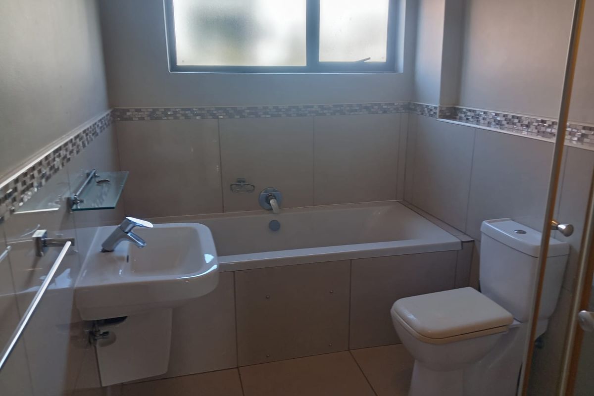 A functional bathroom featuring a built-in bathtub, wall-mounted basin, and toilet with neutral wall tiling and a decorative mosaic border.
